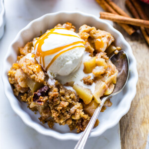 Apple crumble in a single serving dish with ice cream and caramel sauce on top.