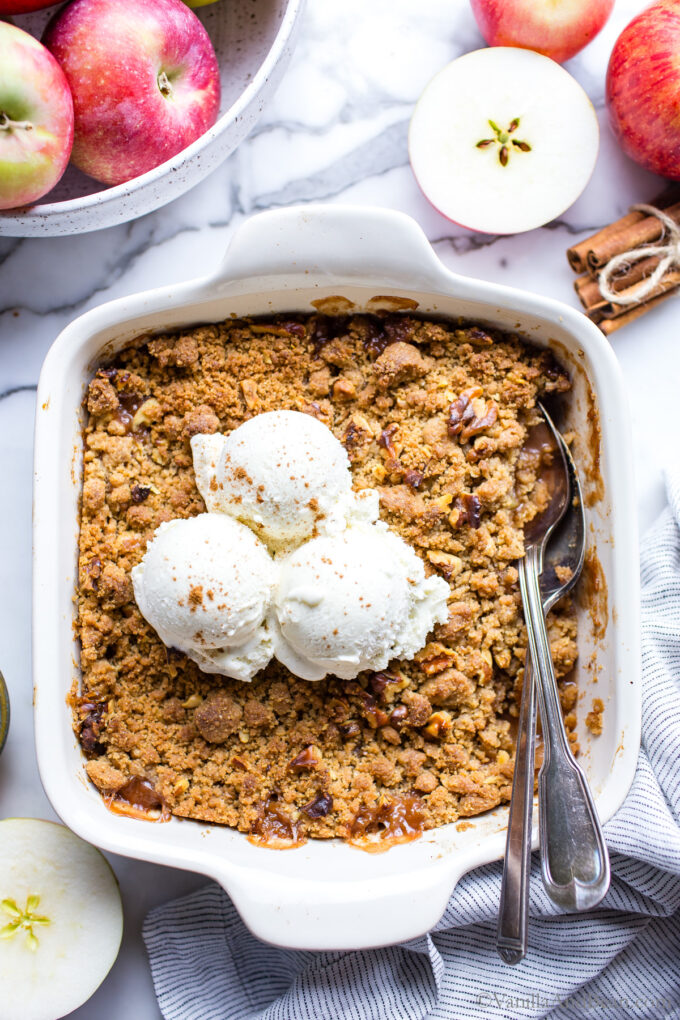 Baked vegan apple crumble in a baker with two spoons on the side and ice cream on top!