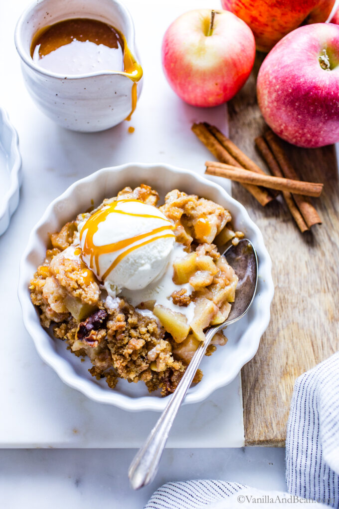Apple crumble in a single serving dish with ice cream and caramel sauce on top.