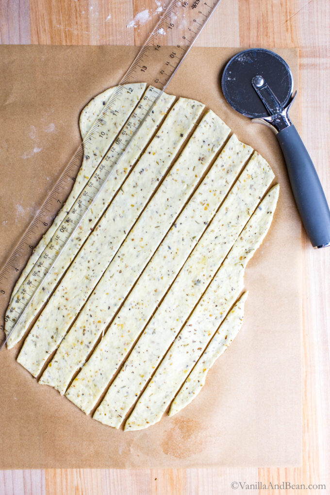 Cutting olive oil sourdough discard crackers with a pizza wheel.