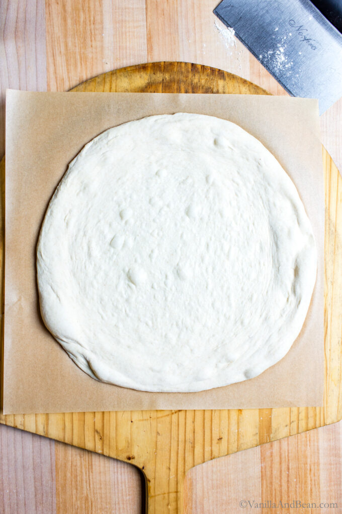 Shaped sourdough discard pizza dough on a piece of parchment.