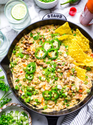 Creamy and warm Black Eyed Pea Dip with Cream Cheese in a skillet garnished with fresh jalapenos, green onions, parsley and tortilla chips.