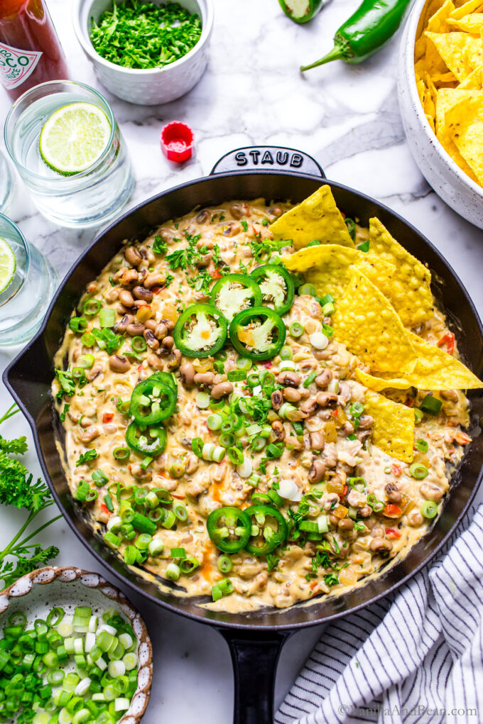 Creamy and hot Black Eyed Pea Dip with Cream Cheese in a skillet garnished with fresh jalapenos, green onions, parsley and tortilla chips.