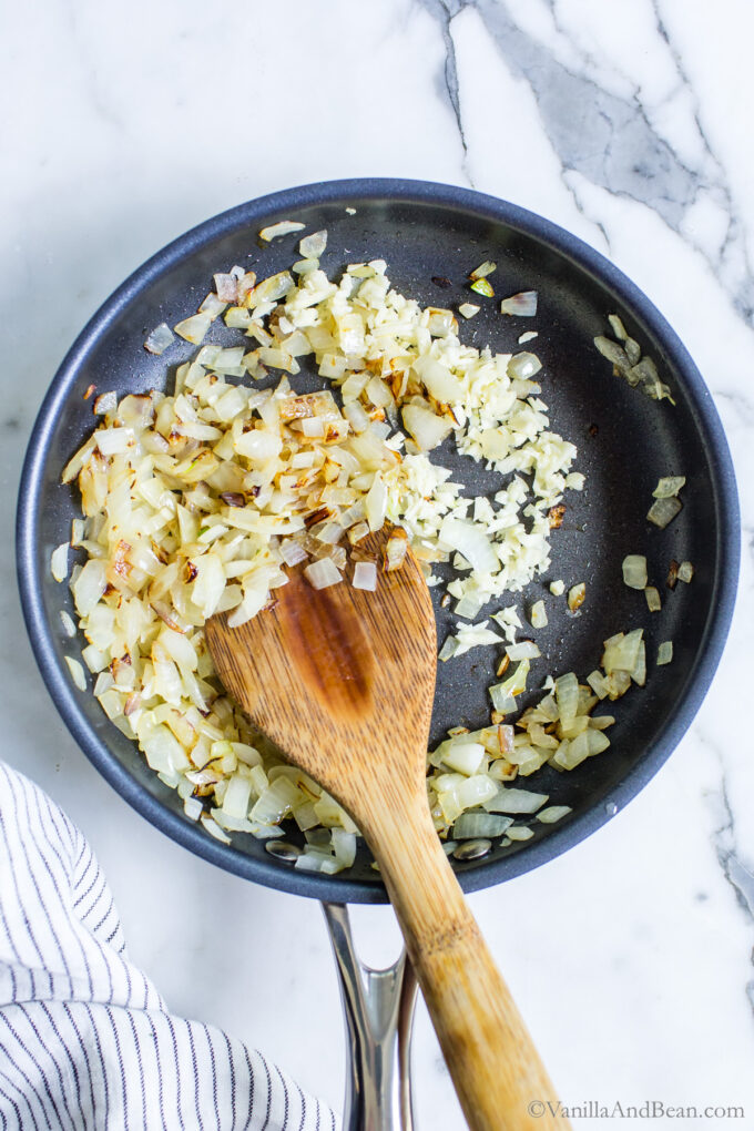 Sauted onions in a pan with a wood spoon.