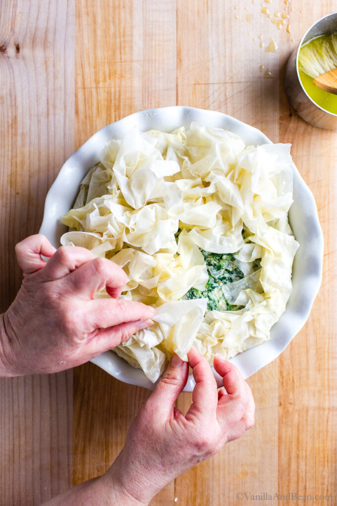Buttered and crumpled phyllo dough being placed on top of the spinach pie.