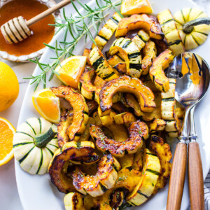 Butter roasted delicata squash on a serving platter with spoons on the side.