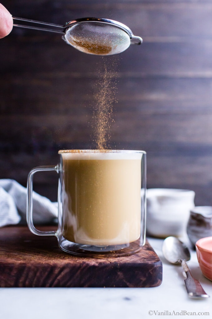 Sprinkling cinnamon over the top of hot chai tea latte.