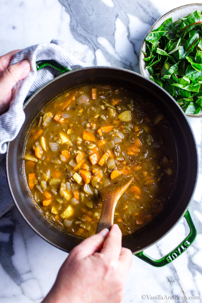 Stirring the vegetarian french lentil soup with a wooden spoon.