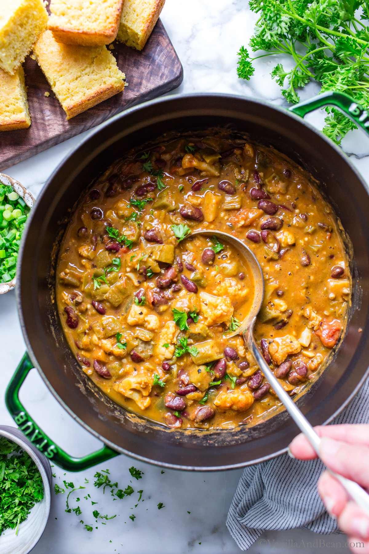 Vegetable gumbo recipe in a Dutch oven with a ladle scooping up a portion.