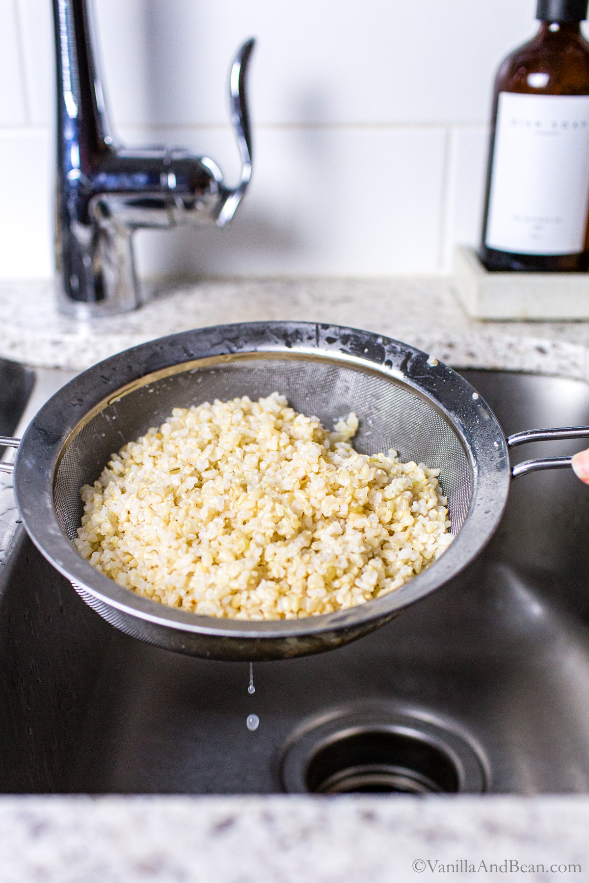 Draining brown rice through a fine strainer in the sink.
