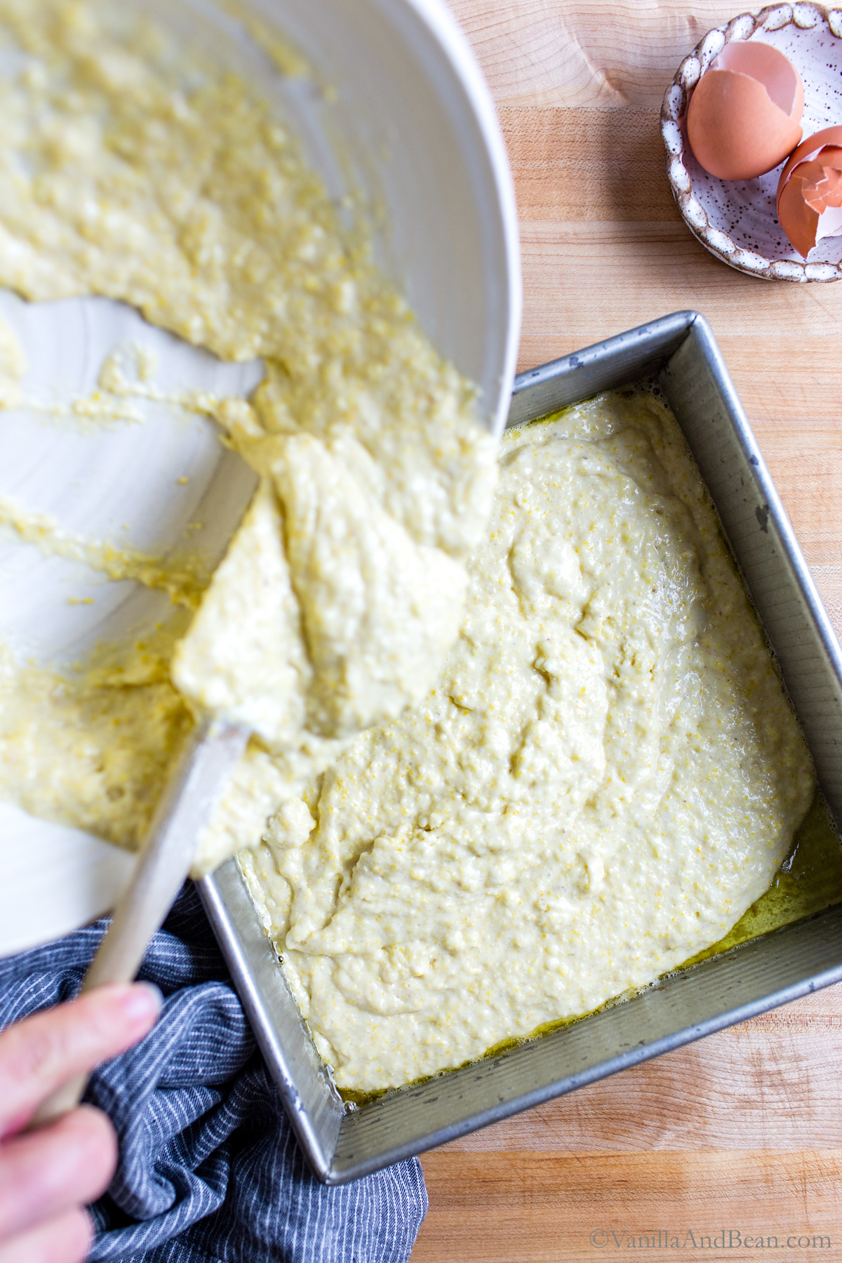 Scraping the cornbread batter into a hot buttered.