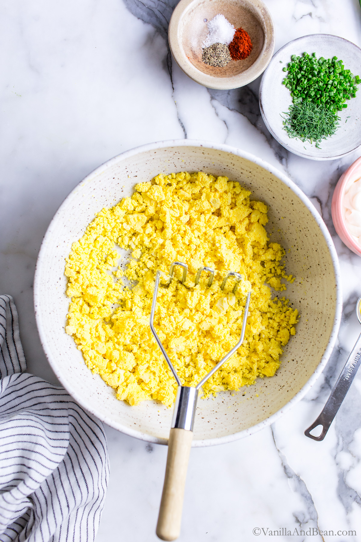 Hard cooked egg yolks in a bowl being mashed with a potato masher.