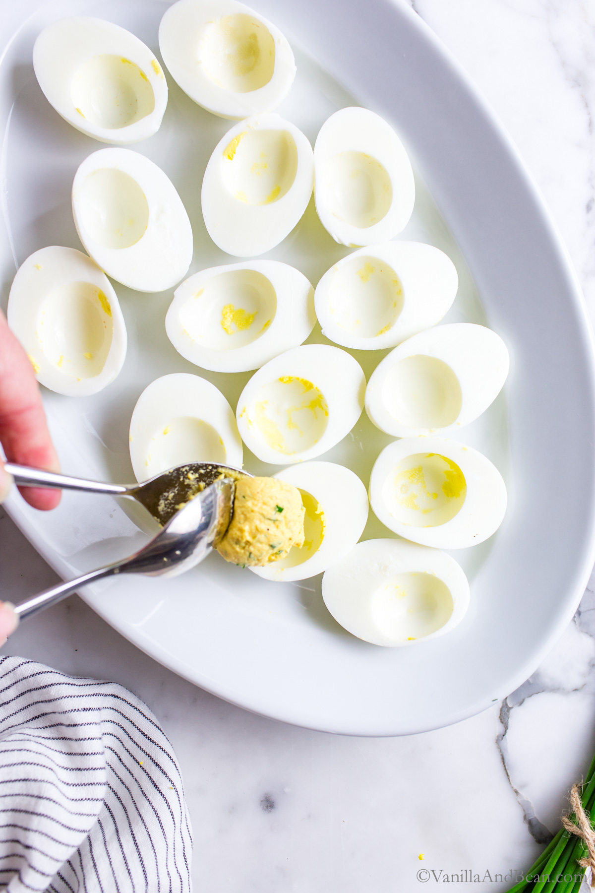 Hard cooked egg whites on a platter with the egg yolk mixture being spooned in the egg white void.