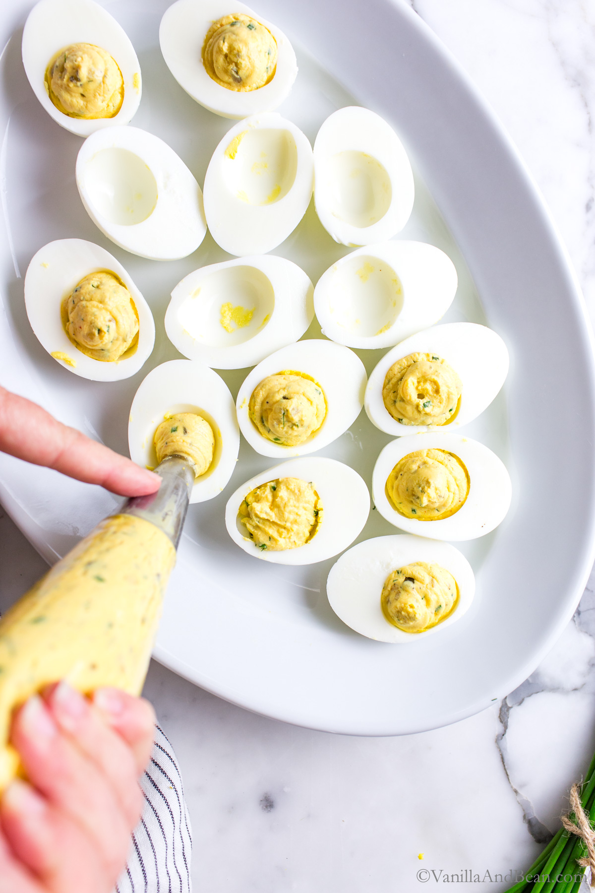 Hard cooked egg whites on a platter with the egg yolk mixture being piped in the egg white void.