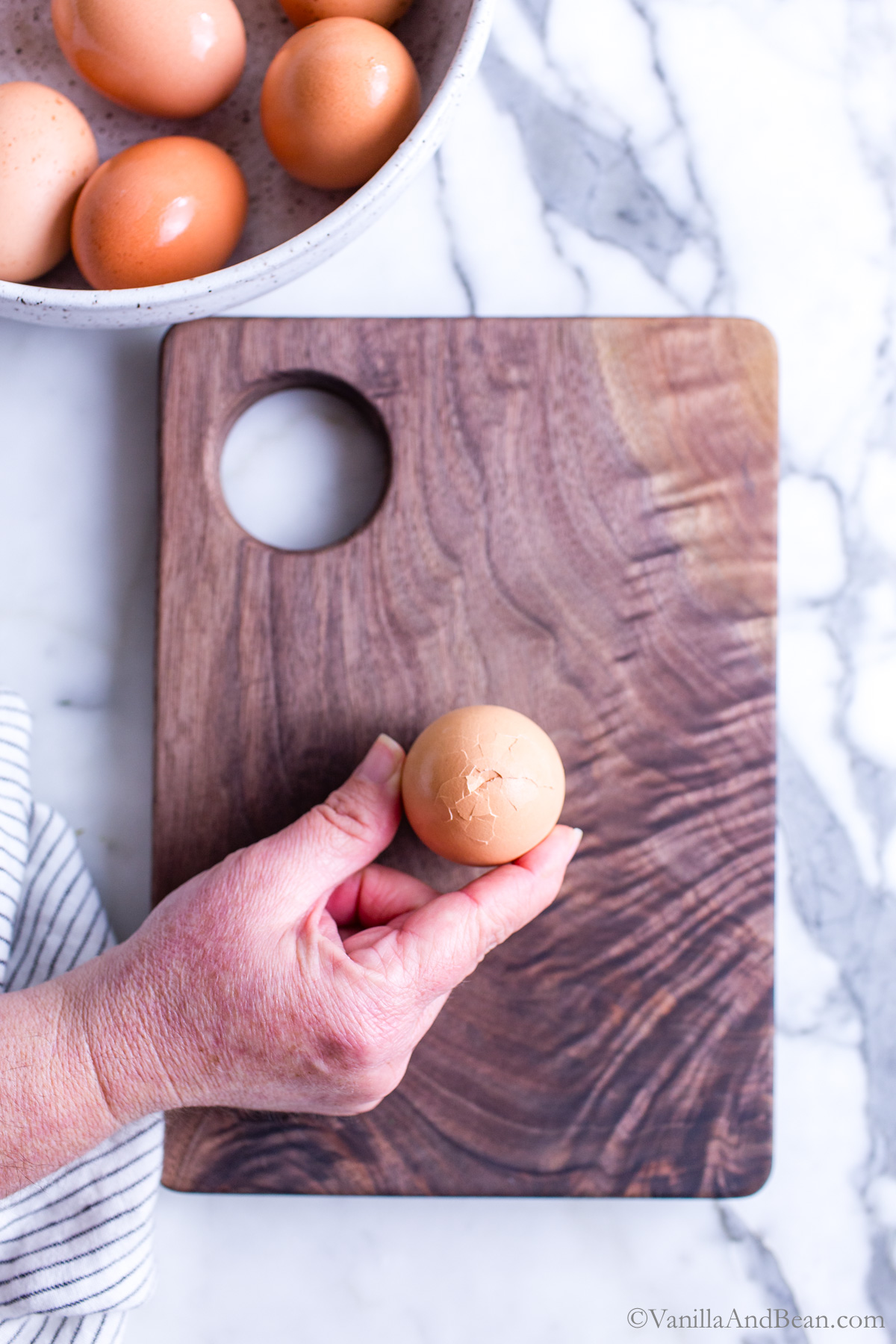 Cracking the wide end of a hard boiled egg on a cutting board.