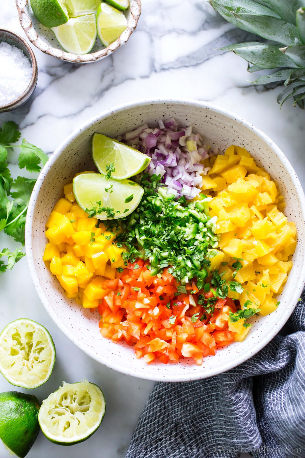 Mango Pineapple Salsa ingredients in a bowl before stirring, garnished with large lime wedges.