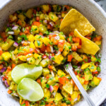 Stirred Mango Pineapple Salsa ingredients in a bowl garnished with tortilla chips and lime wedges.