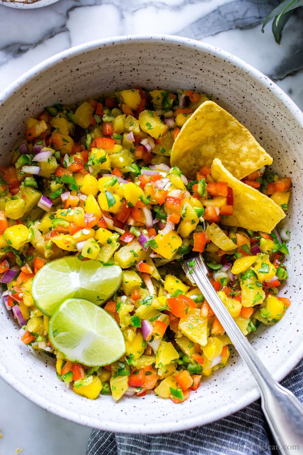 Stirred Mango Pineapple Salsa ingredients in a bowl garnished with tortilla chips and lime wedges.