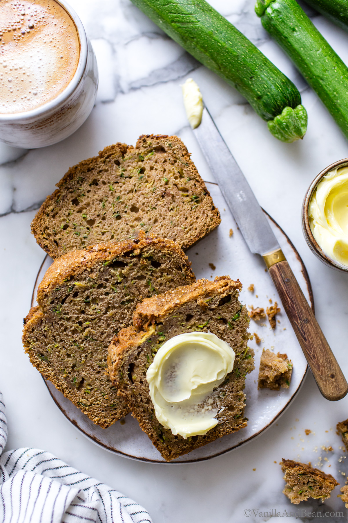 Three slices of baked sourdough zucchini bread on a plate with a smear of butter.