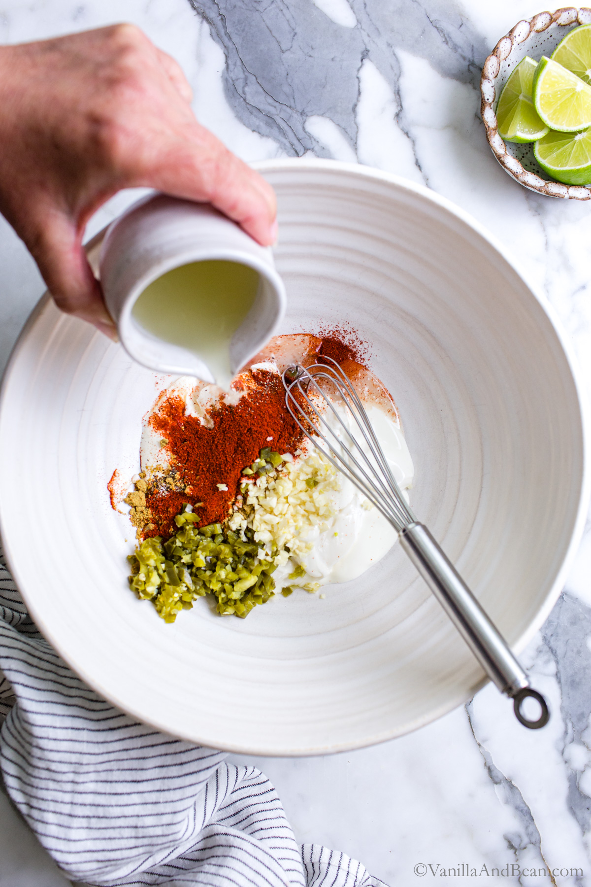 Street corn mayo dressing in a large bowl with lime juice being poured into the bowl.