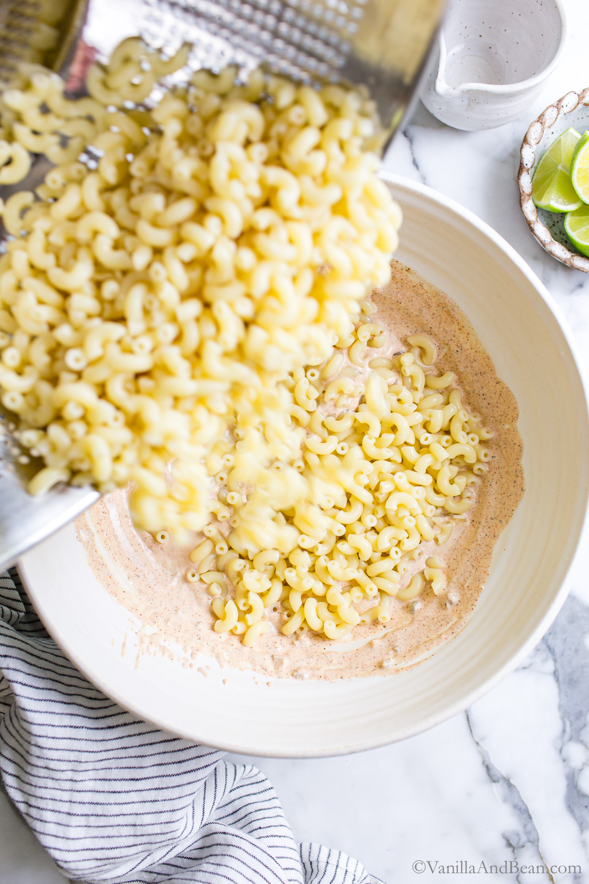 Mayo dressing and macaroni pasta being poured into a bowl.