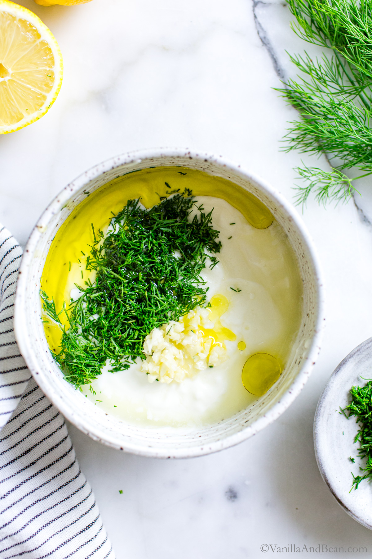 Yogurt and Dill Sauce in a bowl with ingredients showing on top: dill, garlic, lemon, olive oil.
