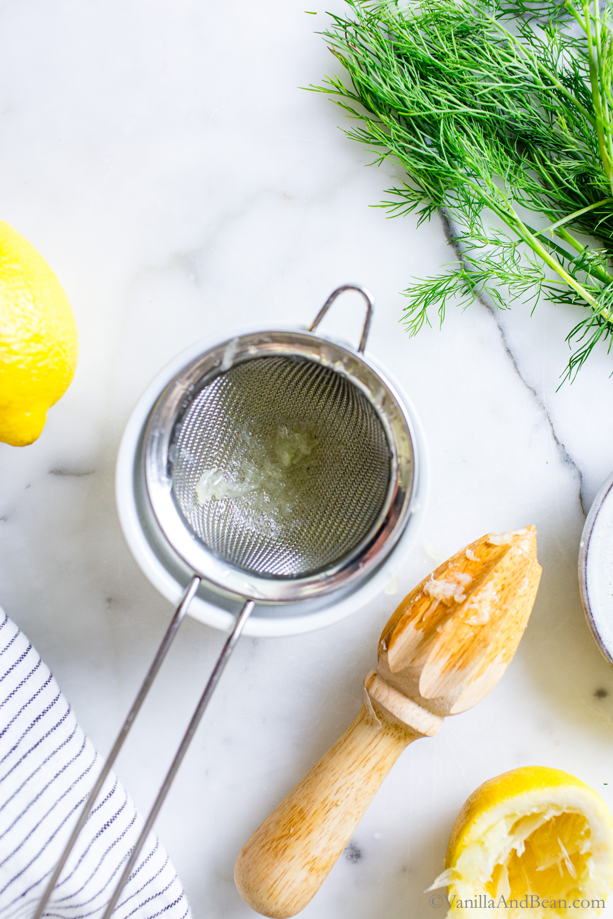 Juiced lemon in a bowl with a sieve over the top and a lemon juicer set to the side.