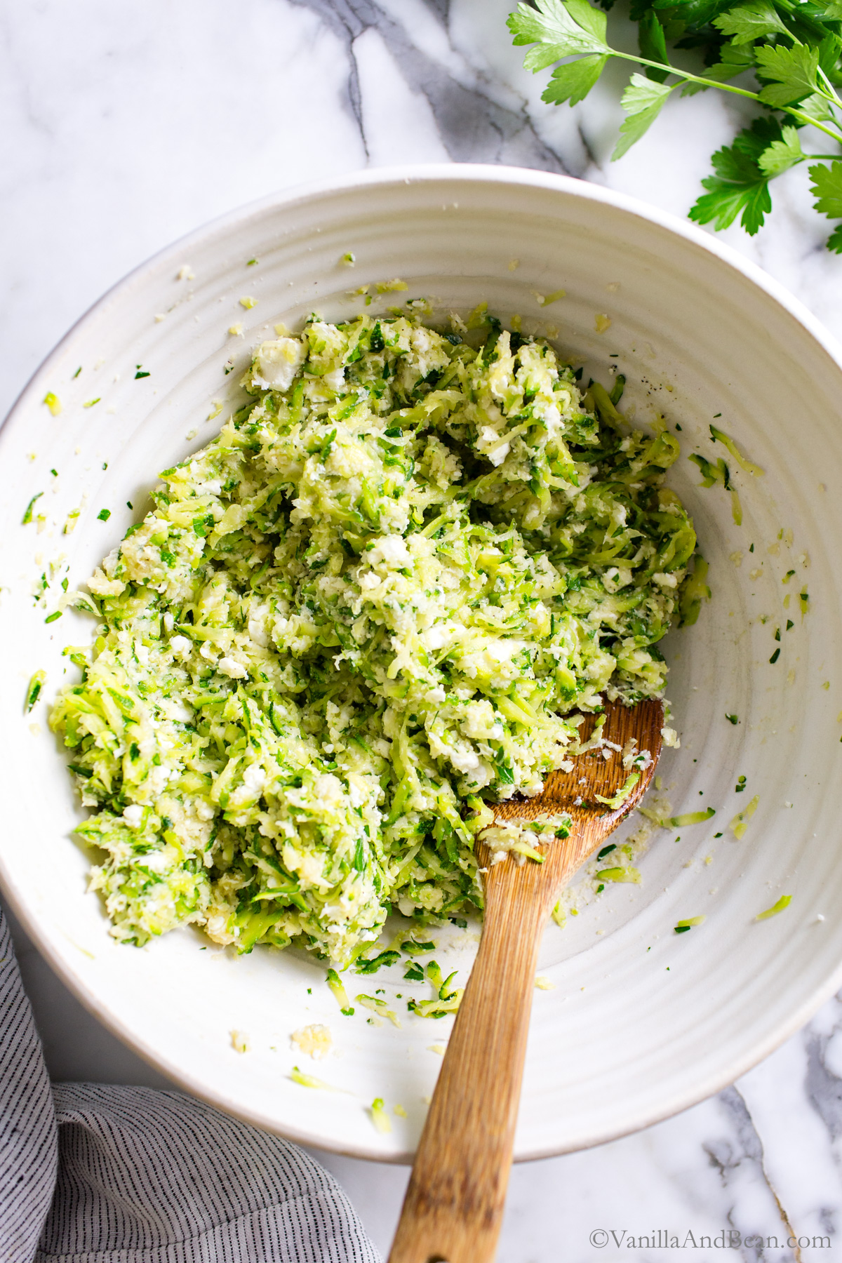 Zucchini Feta fritter ingredients in a large mixing bowl with a wood spoon.