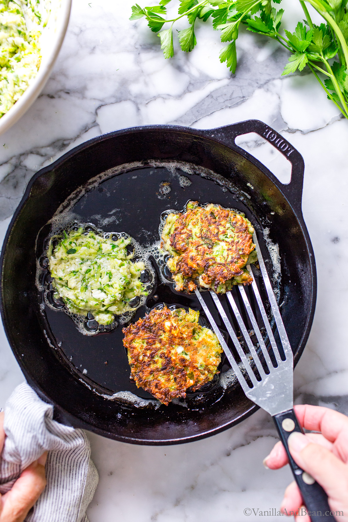 Pan frying Zucchini Feta fritters in a cast iron skillet.
