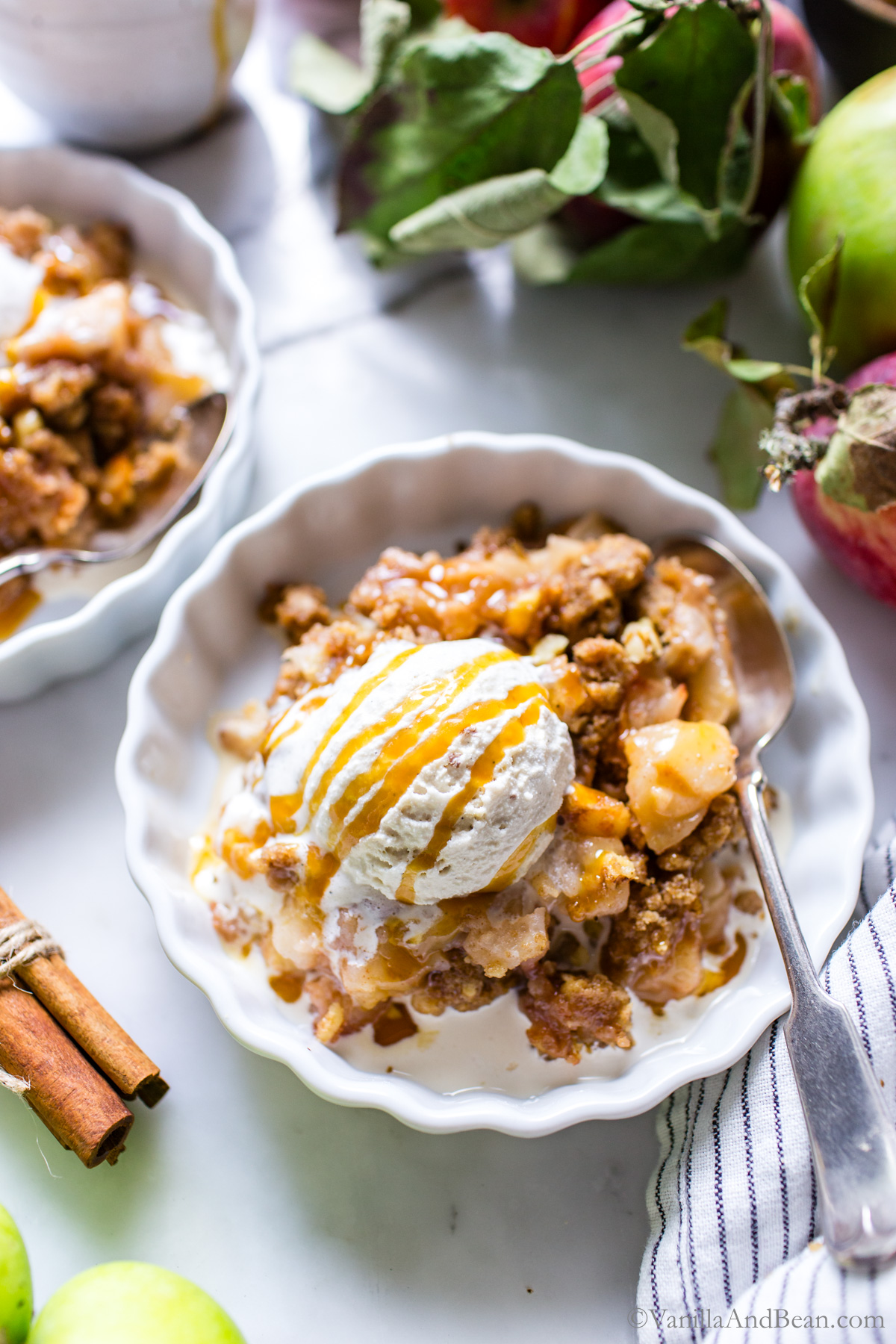 Apple crisp with a dollop of ice cream and drizzle of caramel sauce on a plate.